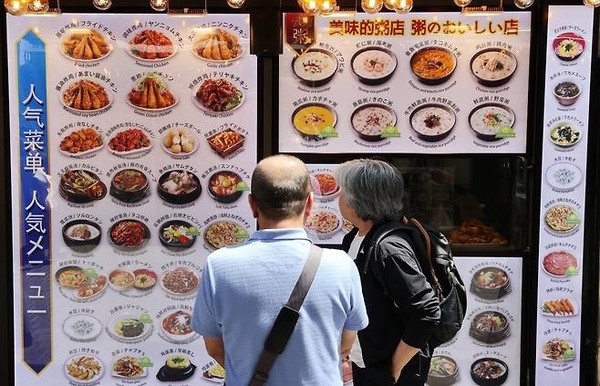 서울 명동에서 외국인 관광객들이 외국어로 된 메뉴를 살펴보는 모습 (출처_연합뉴스)